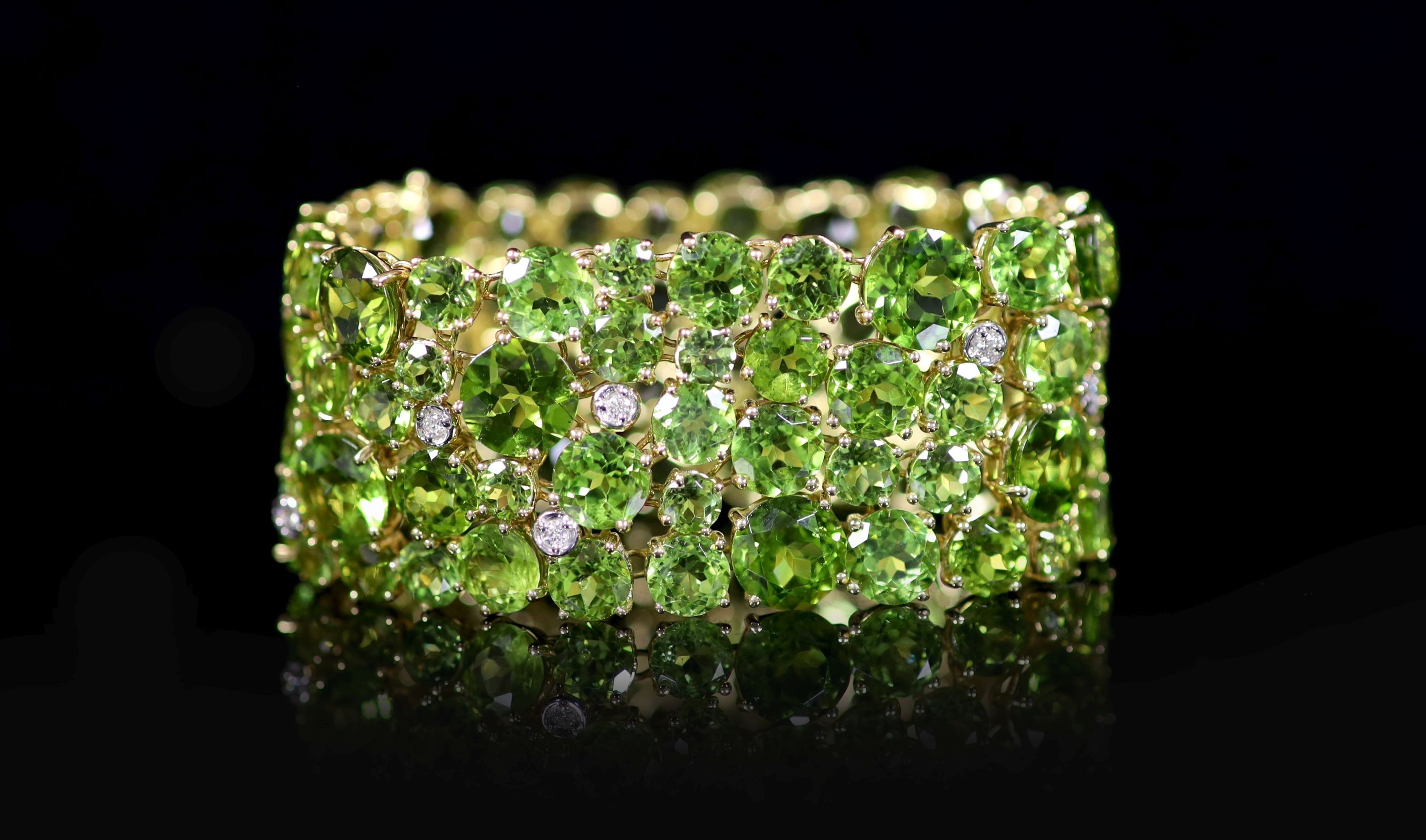 A Continental 18k gold and graduated round cut peridot encrusted bracelet, with twelve stone diamond random set spacers